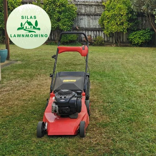 Red push mower on a freshly cut front lawn beside a wooden fence in Glen Eden